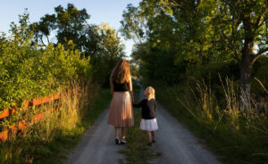 A mother and daughter are walking down a path outside.